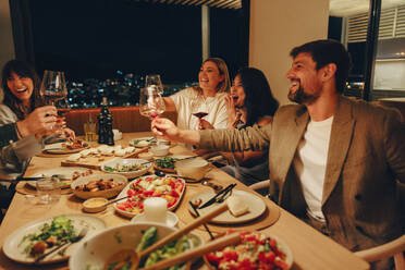 a group of friends smiling and sharing a meal at home in the evening. they are seated around a table filled with food and wine glasses, enjoying conversation and the cozy ambiance.